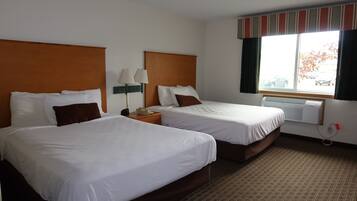 Habitación de hotel con dos camas, una ventana con cortinas, una lámpara y un teléfono en la mesita de noche.