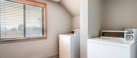 Un lavadero con lavadora y secadora, una ventana con persianas y una ventilación en el techo.
