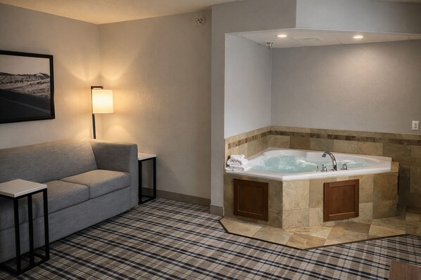 A modern bathroom with a freestanding bathtub, a sofa, and a small table. - AmericInn by Wyndham Dickinson (Dickinson)