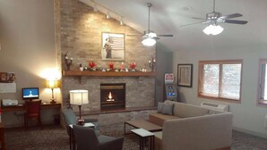 A living room with a fireplace, sofa, armchair, and a desk with a computer. - AmericInn by Wyndham Dickinson (Dickinson)