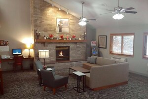 Una sala de estar con chimenea, sofá, sillón y escritorio con computadora.