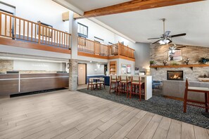 A hotel lobby with a reception desk, seating area, fireplace, and a balcony. - AmericInn by Wyndham Dickinson (Dickinson)