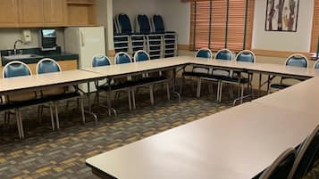 A conference room with a long table, chairs, a refrigerator, a sink, and a window with blinds.