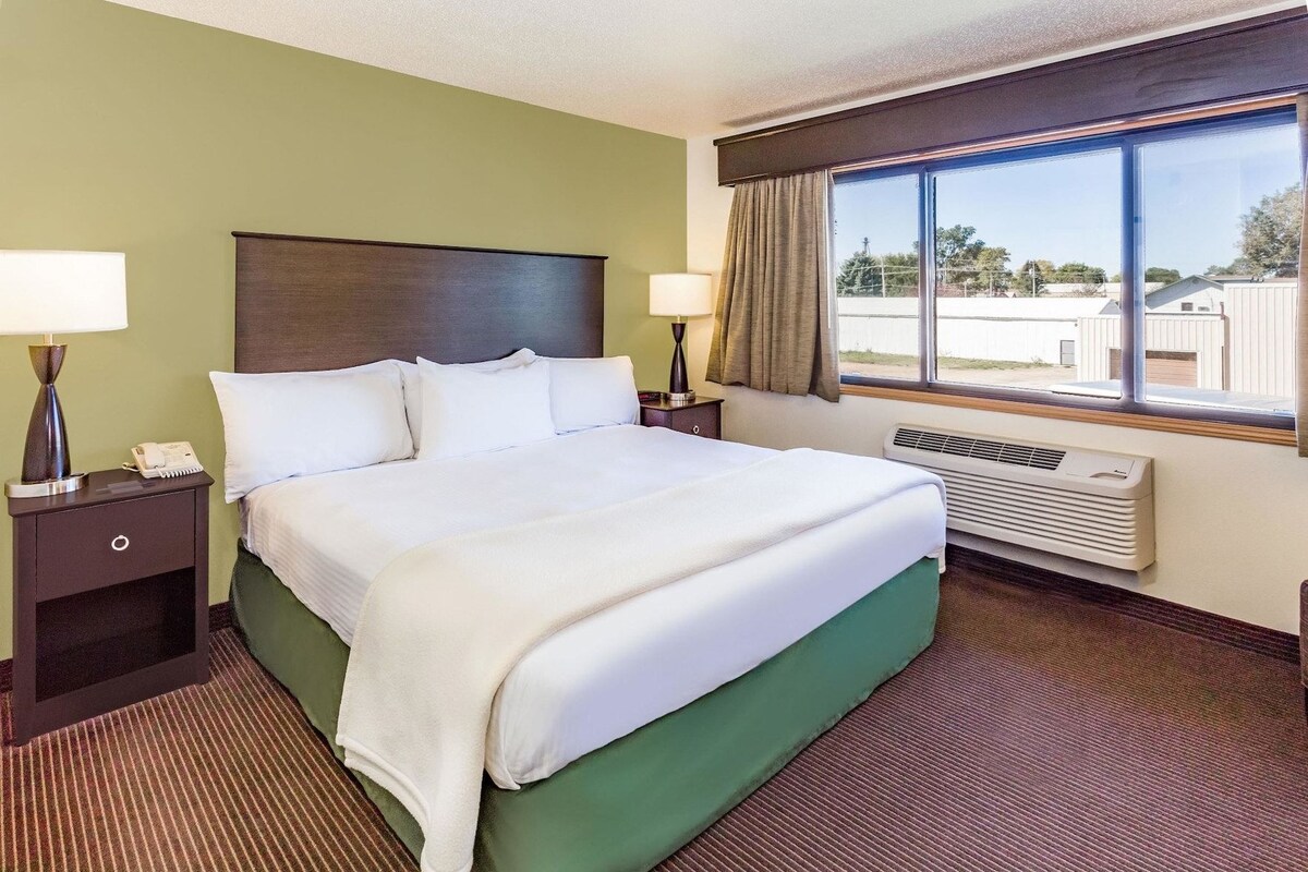 A hotel room with a bed, two bedside tables, a window with curtains, and a wall-mounted heater.