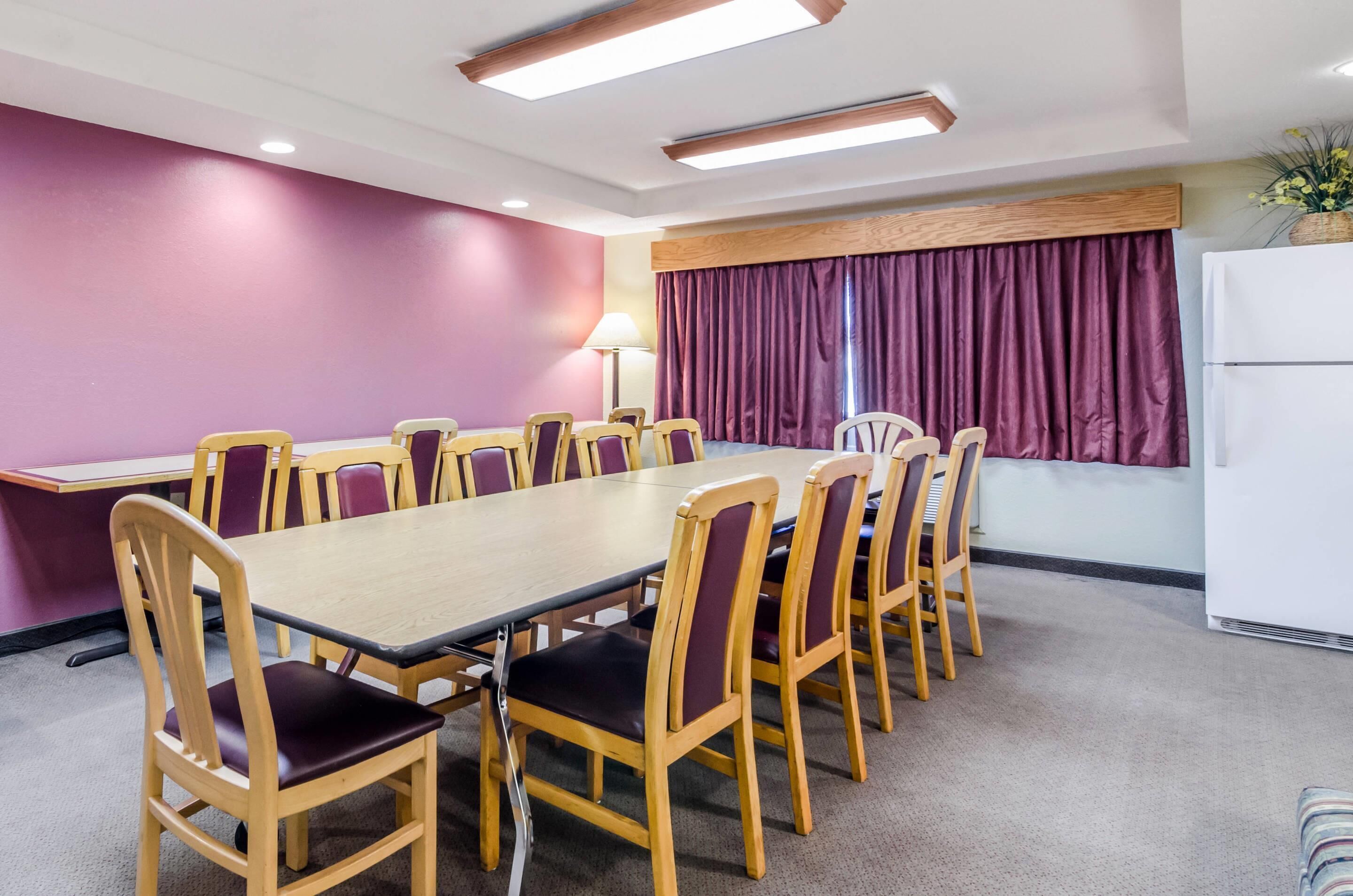 A conference room with a long table and chairs, purple walls, and a window with curtains.