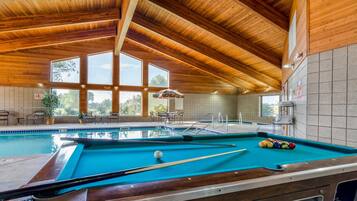 A pool area with a wooden ceiling, a pool table, and a seating area with chairs and a table.