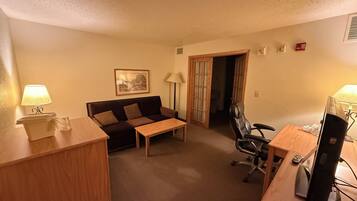 A compact hotel room with a sofa, a small table, a desk with a computer, and a chair.