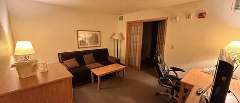A compact hotel room with a sofa, a small table, a desk with a computer, and a chair.