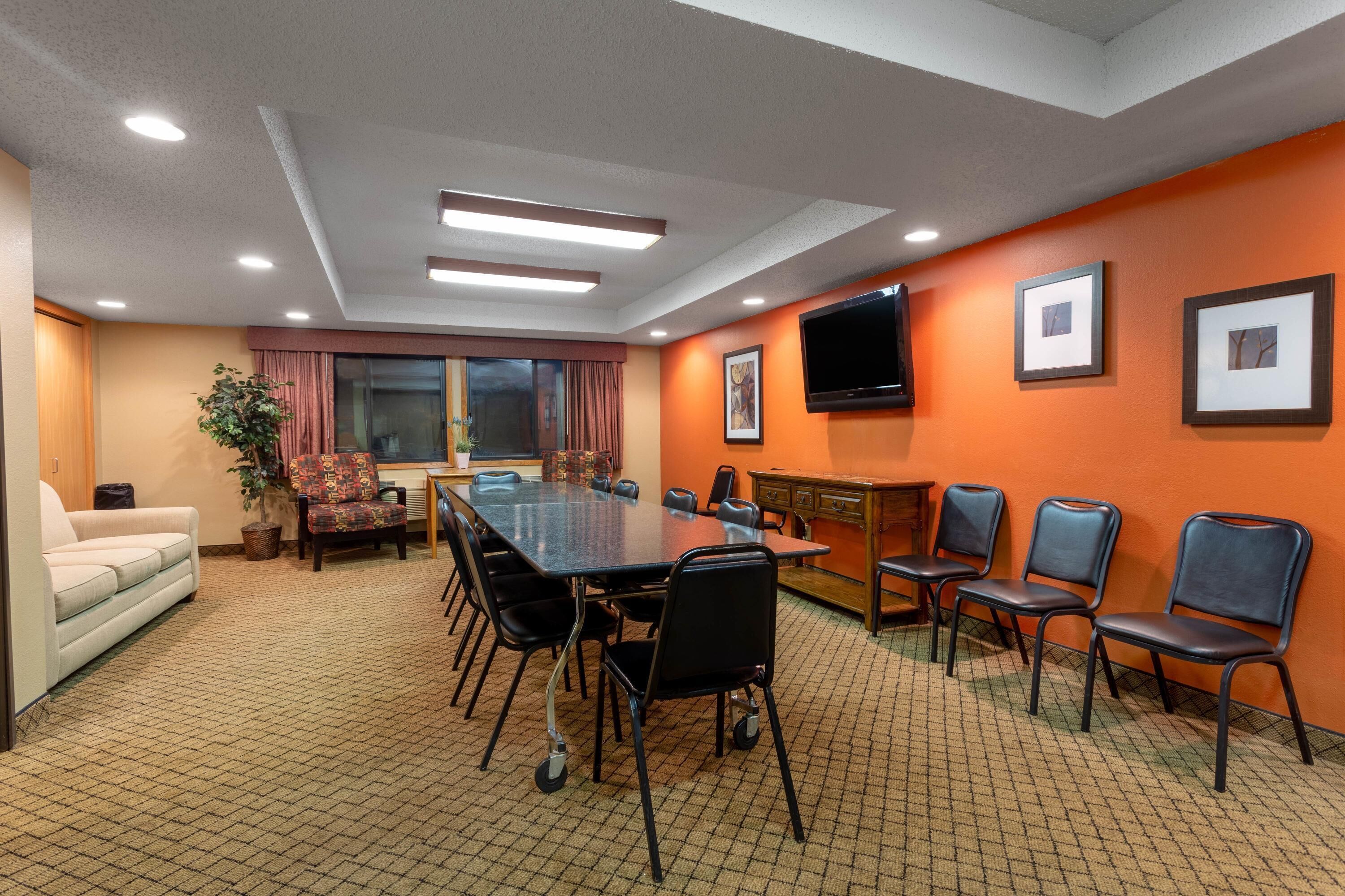 Un salón de conferencias con una mesa grande, sillas, un sofá, un televisor y cuadros en la pared.