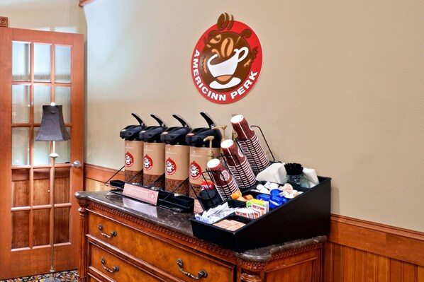 Una estación de café con varios dispensadores, una jarra de café y una variedad de tazas y mugs.