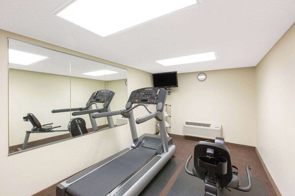 Un gimnasio con cinta de correr, elíptica y bicicleta estática, un espejo grande y un televisor en la pared.
