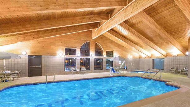 Una piscina interior con vigas de madera, paredes con baldosas y zonas de estar.