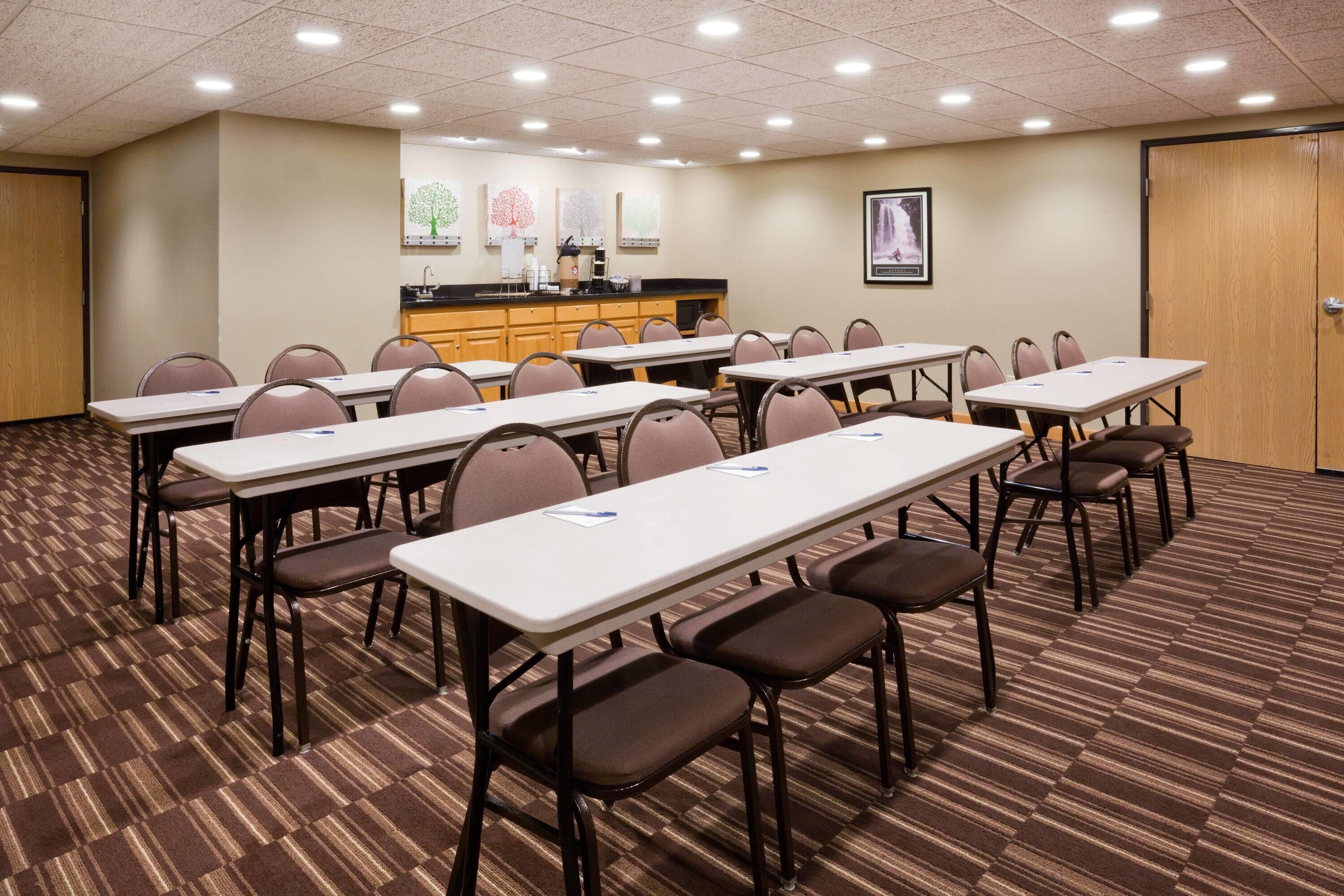 Un salón de conferencias con varias mesas y sillas, una kitchenette y una puerta.