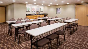 Un salón de conferencias con varias mesas y sillas, una kitchenette y una puerta.