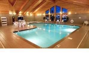 Une piscine avec une terrasse carrelée, des chaises longues et un plafond en bois.
