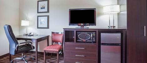 Habitación de hotel con escritorio, silla, televisor, refrigerador y lámpara.