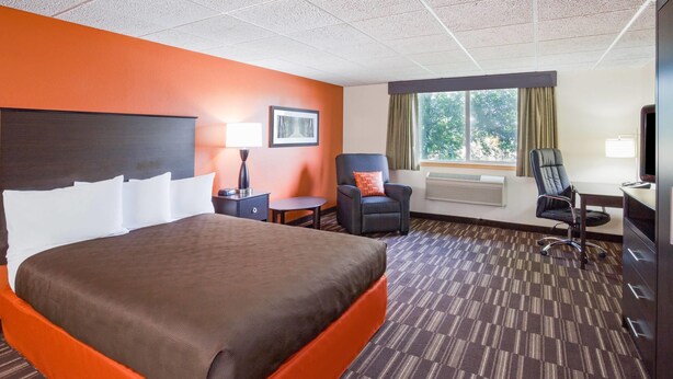 A hotel room with a large bed, a desk, a chair, a window with curtains, and a picture on the wall. - AmericInn by Wyndham Sartell (Sartell)