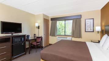Una habitación de hotel con una cama grande, televisor, escritorio con computadora, silla y aire acondicionado.