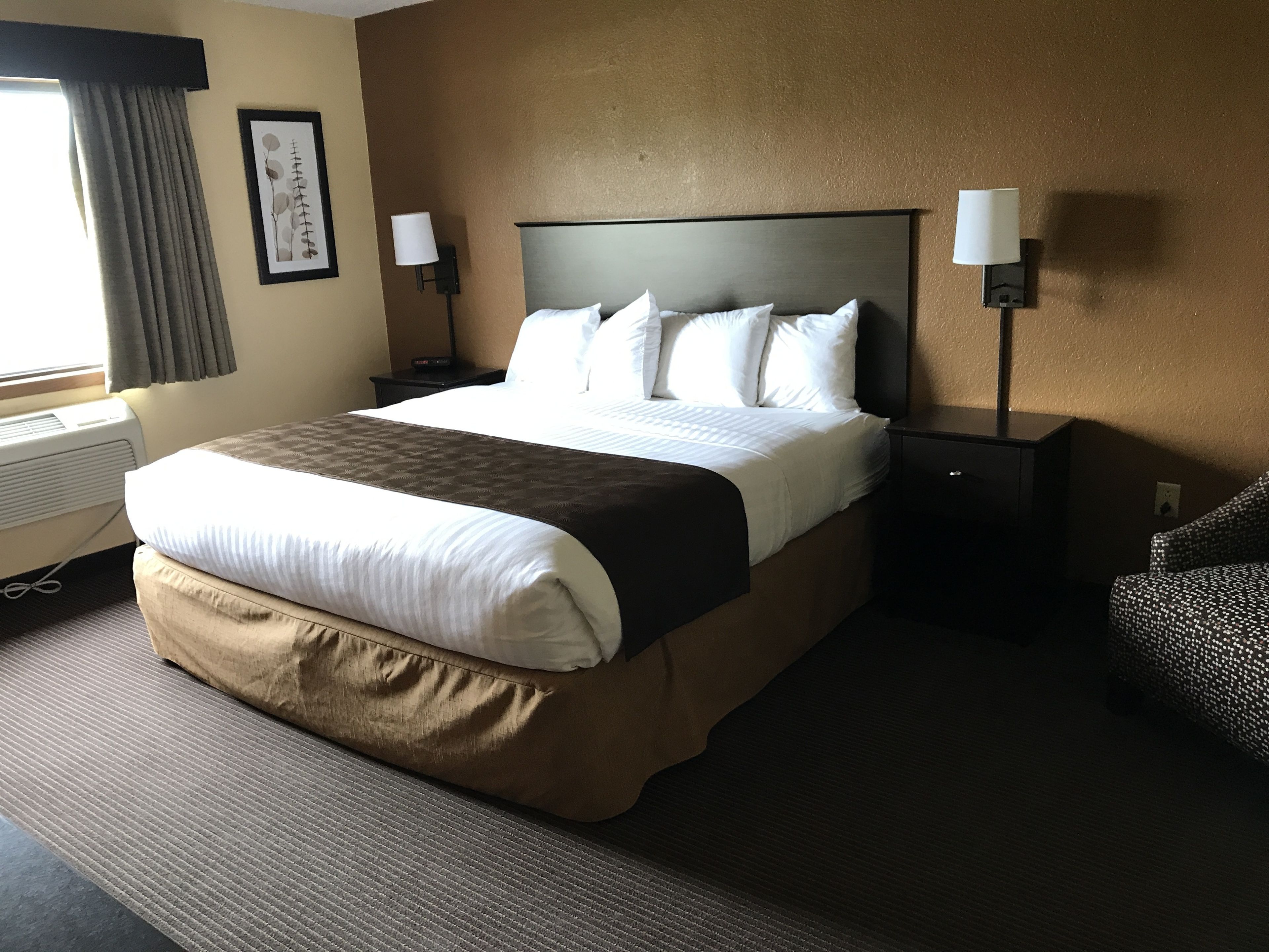 A hotel room with a large bed, two bedside tables, a wall-mounted lamp, and a framed picture.