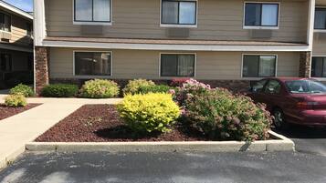 A two-story building with a parking lot, a red car parked in front, and a landscaped garden with various shrubs and flowers.