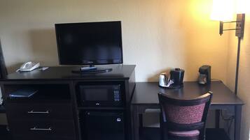 Quarto de hotel com escrivaninha, televisão, micro-ondas, máquina de café e uma cadeira.