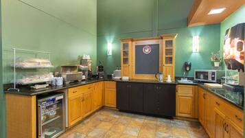 Una cocina con pared verde, armarios de madera, encimera negra y una cafetera.