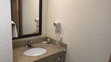 A bathroom with a granite countertop sink, a mirror, a hairdryer, and a towel rack.
