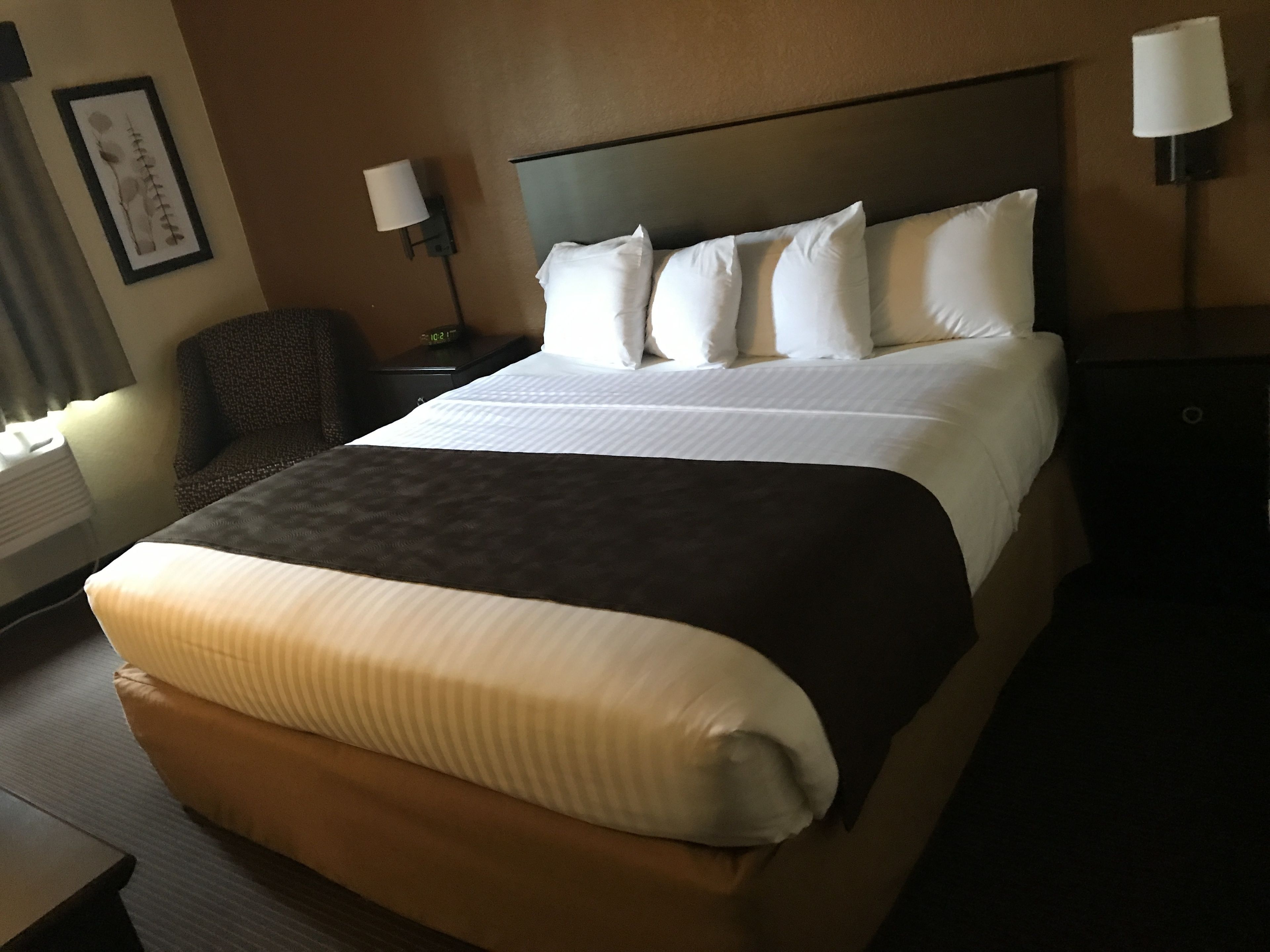 Een hotelkamer met een groot bed, twee bedlampen, een stoel en een foto in een lijst aan de muur.