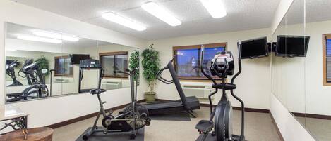 Un gimnasio con equipo de ejercicio, un espejo grande y un televisor en la pared.