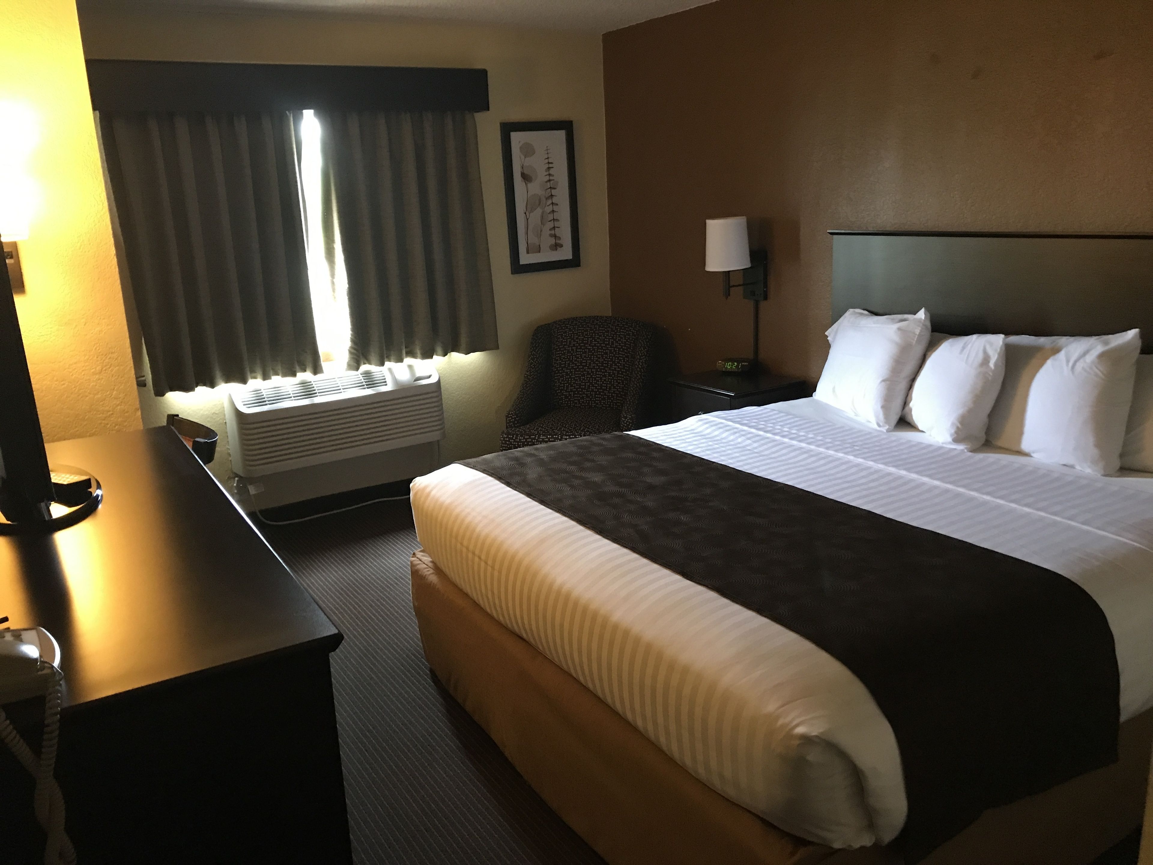 A hotel room with a large bed, a desk, a chair, a lamp, and a window with curtains.