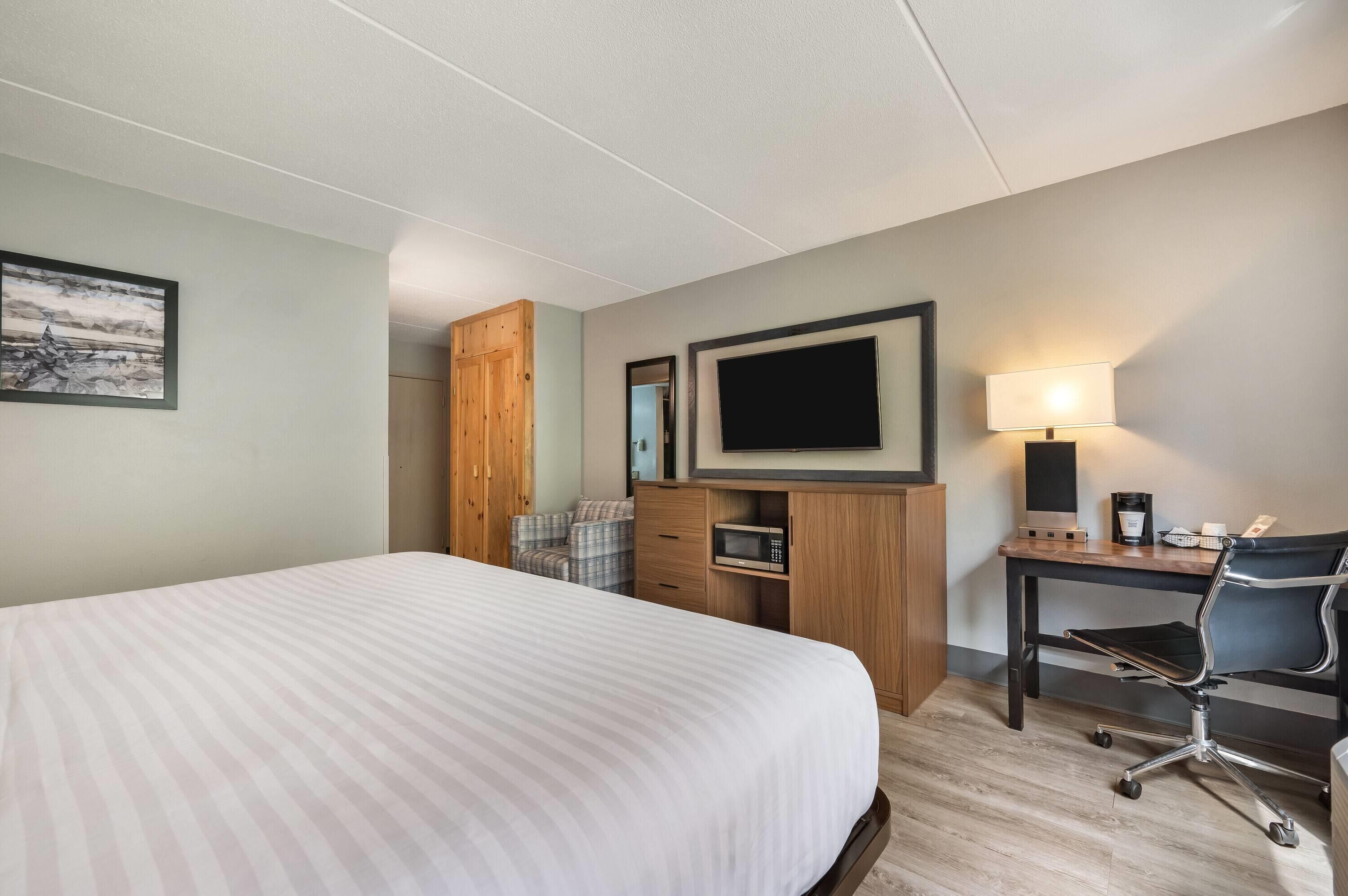 A hotel room with a large bed, a desk with a chair, a television, a microwave, and a coffee maker.