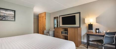 A hotel room with a large bed, a desk with a chair, a television, a microwave, and a coffee maker.