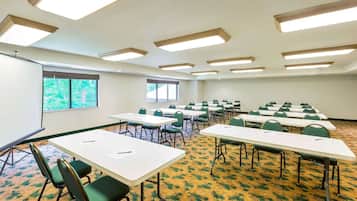 A conference room with multiple tables and chairs, a projector screen, and large windows.