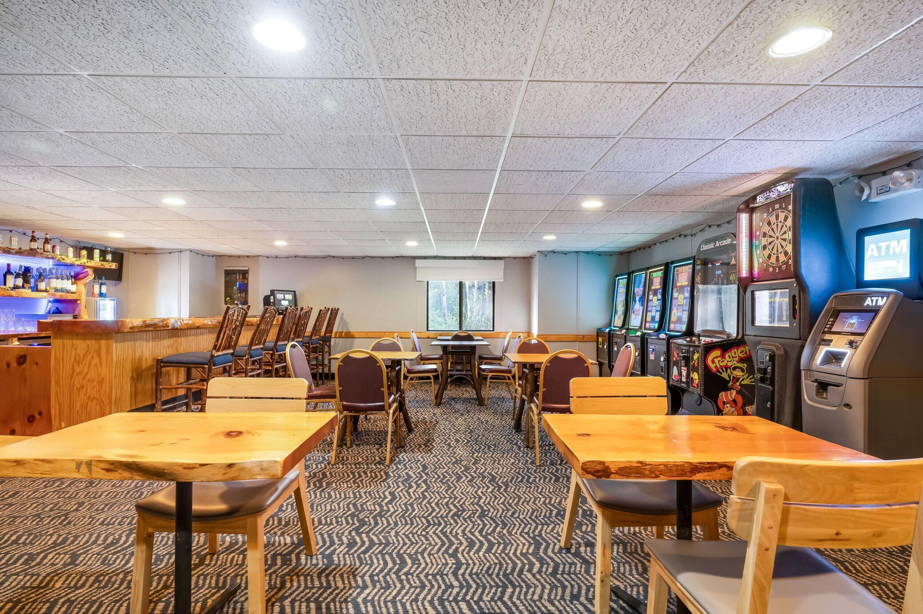 A room with wooden tables and chairs, an ATM, and slot machines.