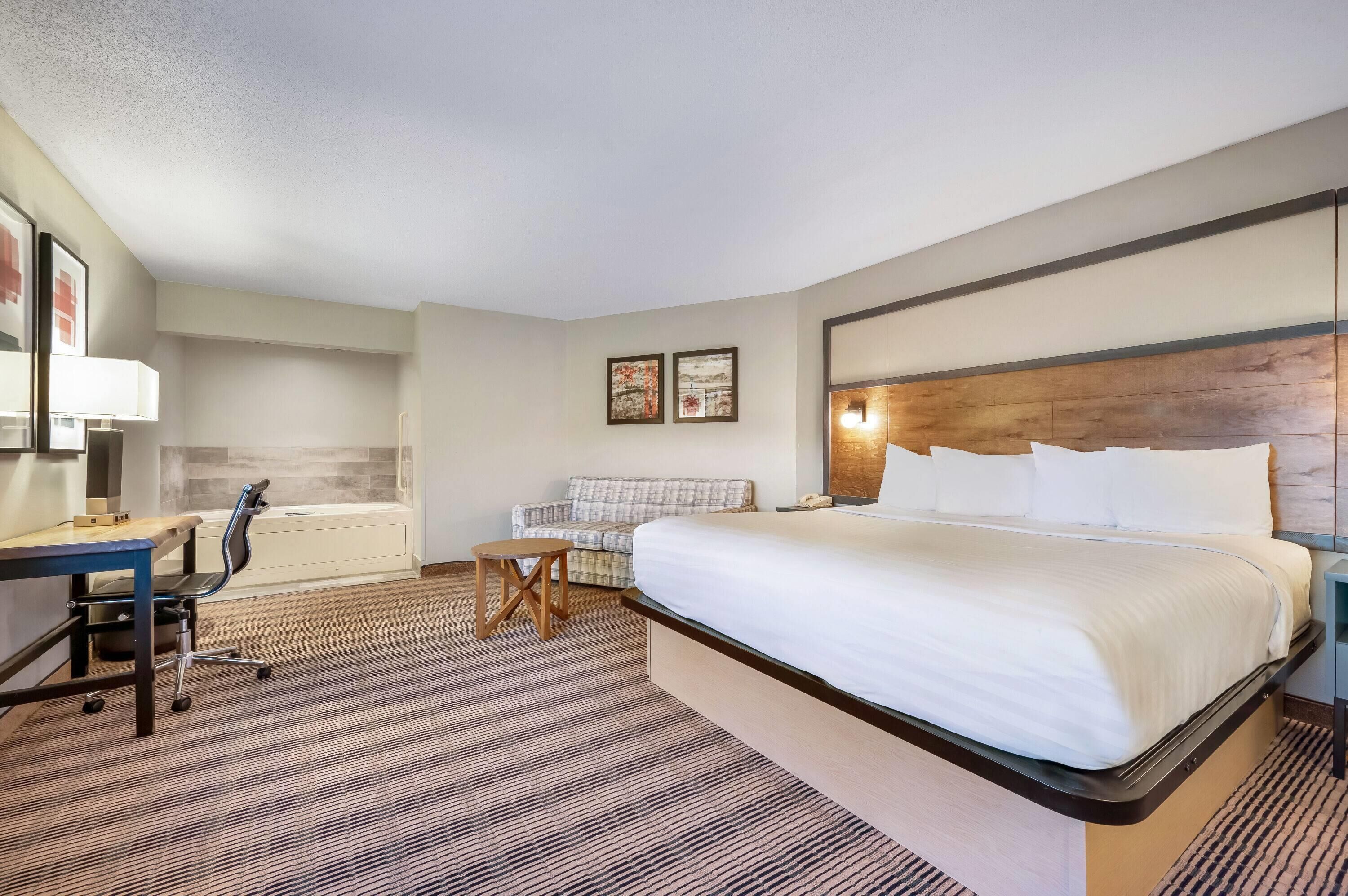 A hotel room with a bed, desk, chair, and a small table.