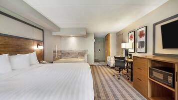 A hotel room with a large bed, a desk with a chair, a microwave, a TV, and a bathroom with a bathtub.