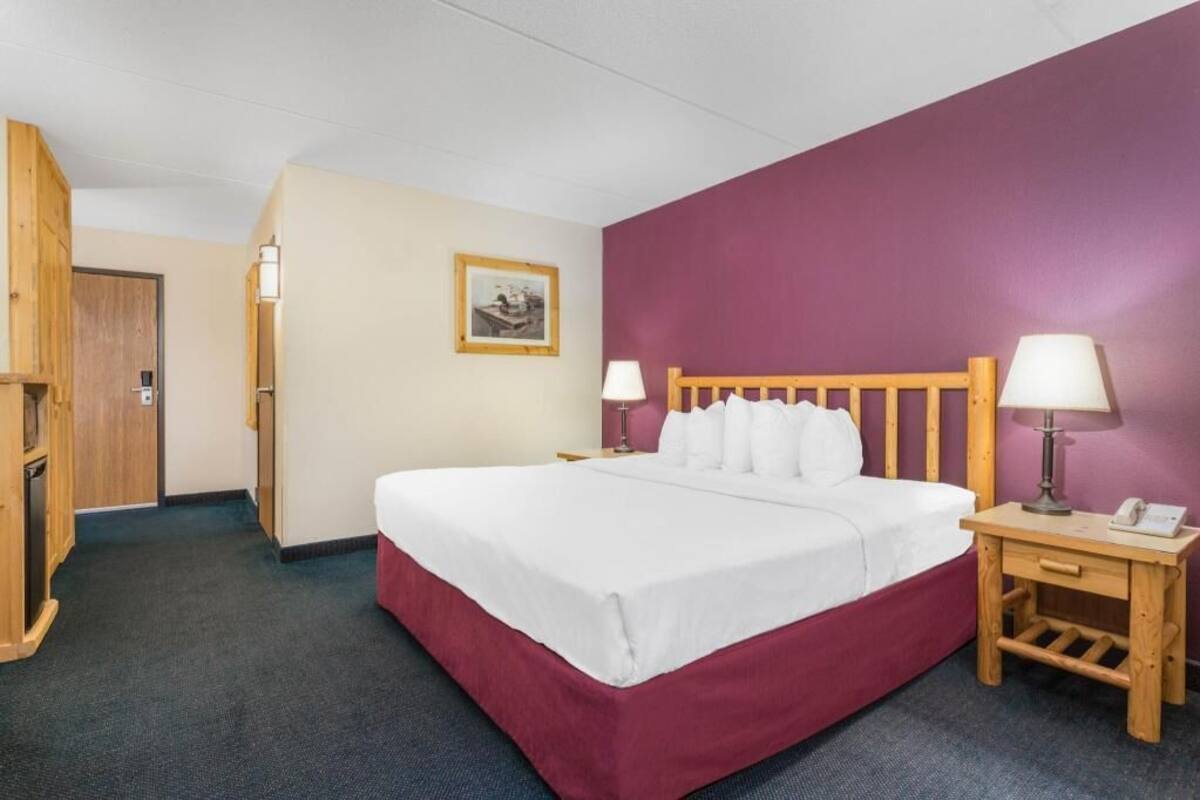 A hotel room with a bed, two bedside tables with lamps, a wooden wardrobe, and a framed picture on the wall.