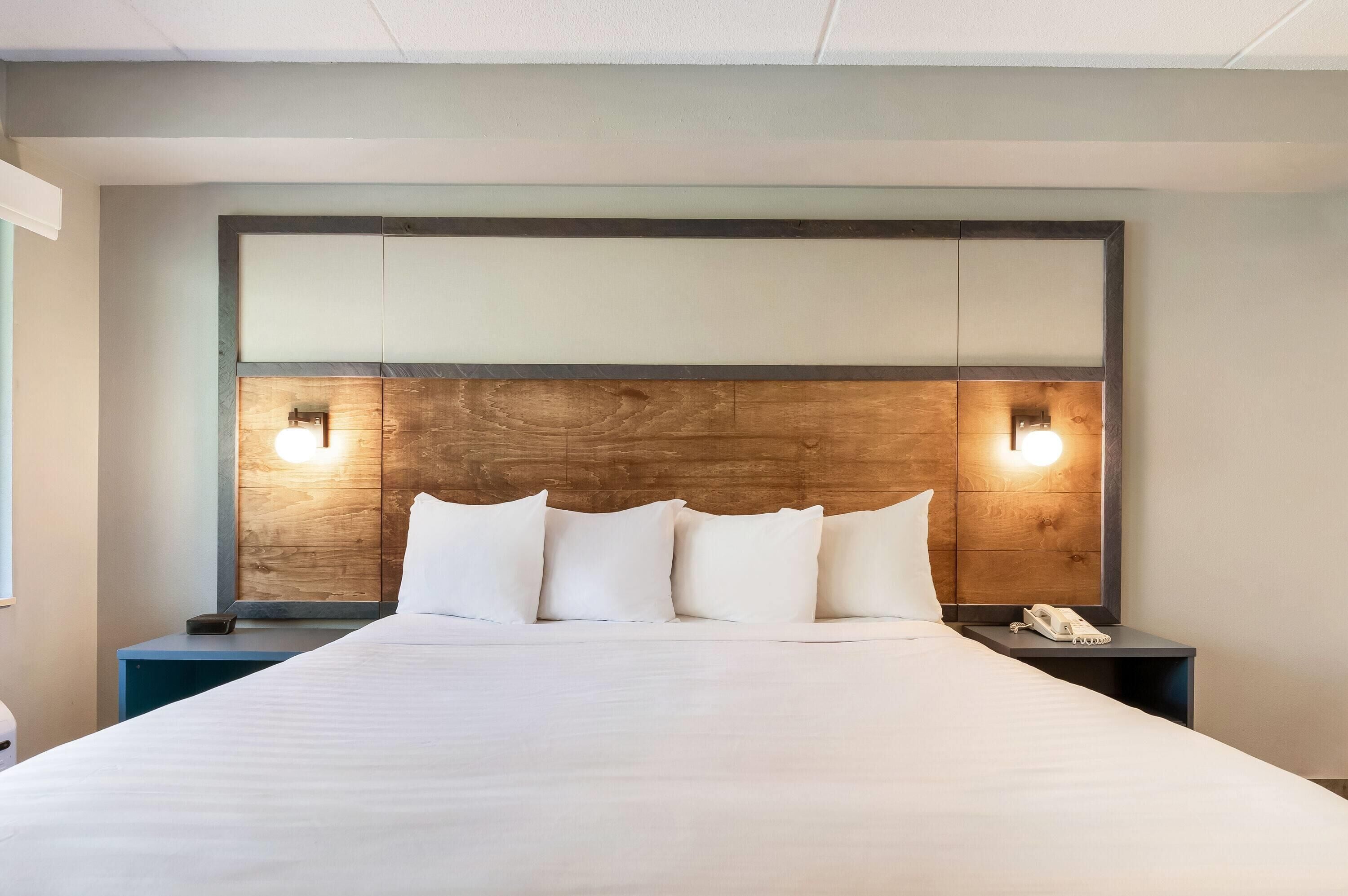 A hotel room with a large bed, a wooden headboard, two bedside tables, and a nightstand with a phone.