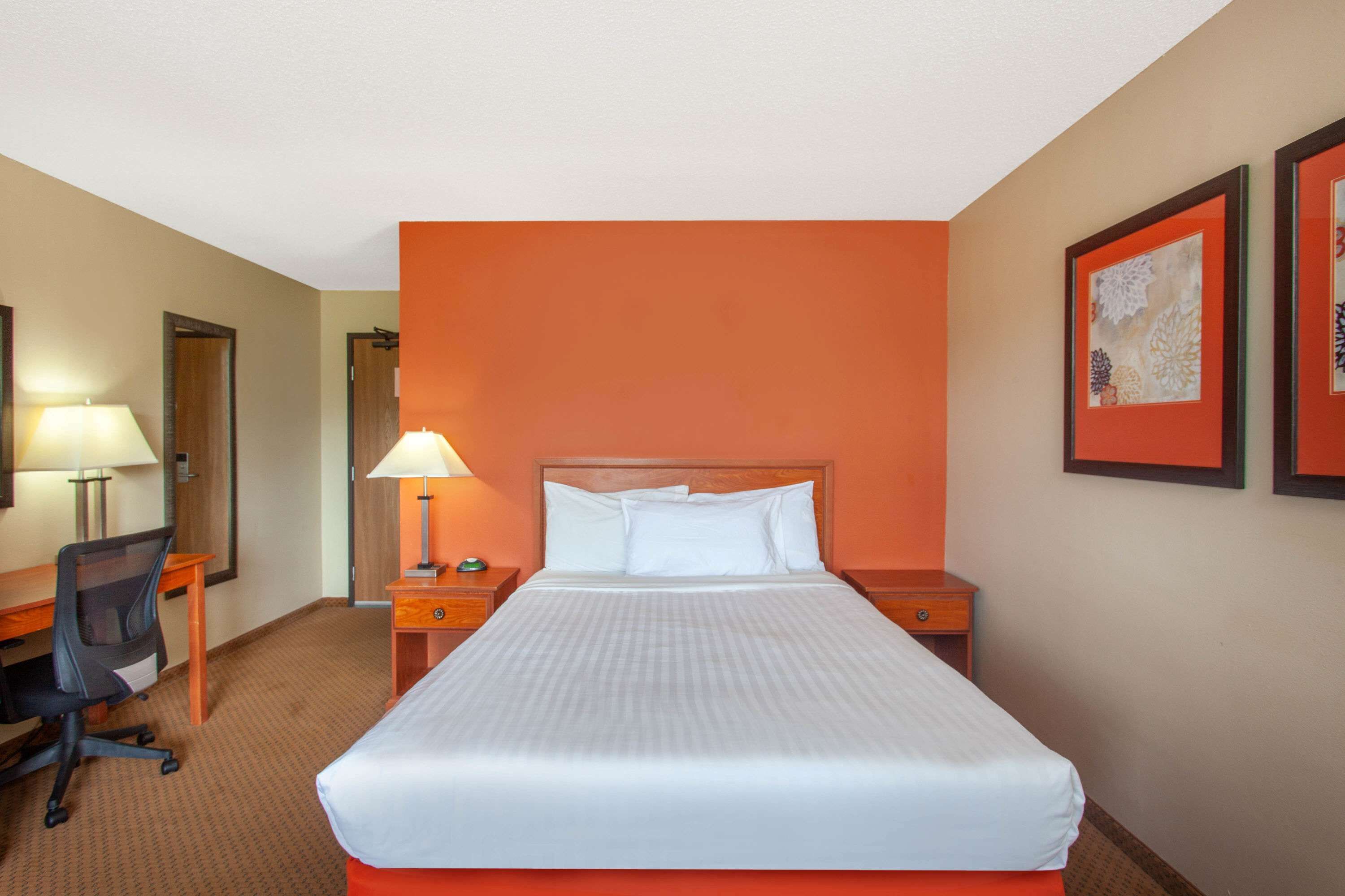Una habitación de hotel con una cama grande, dos mesitas de noche, un escritorio y una silla.