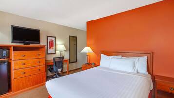 A hotel room with a large bed, a desk with a chair, a television, and a wardrobe.