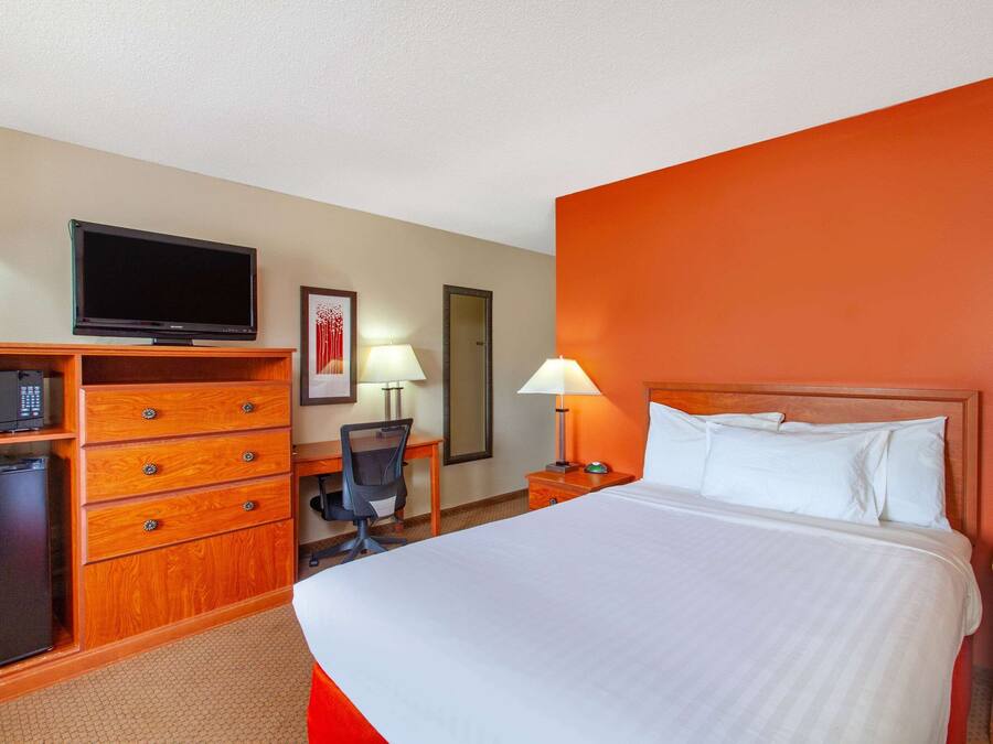 A hotel room with a large bed, a desk with a chair, a television, and a wardrobe.