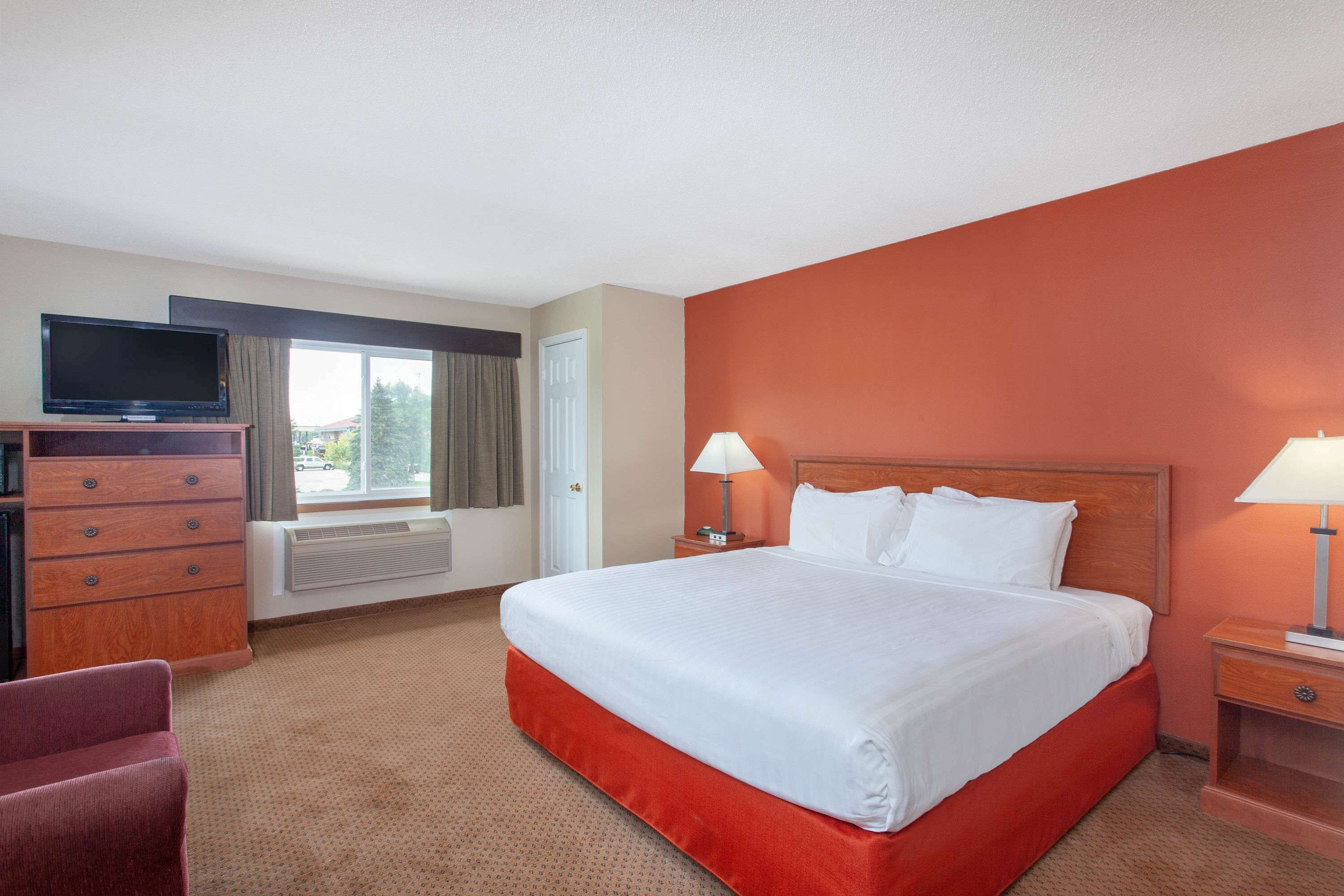 A hotel room with a large bed, a TV on a wooden dresser, two bedside lamps, and a window with curtains.