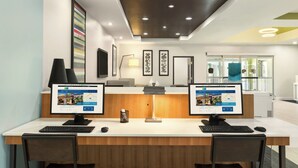 A hotel reception desk with two computer monitors, a desk lamp, and framed artwork on the wall.
