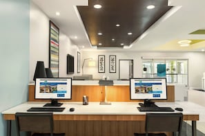 Een receptiebalie van een hotel met twee computerschermen, een bureaulamp en lijstwerk aan de muur.
