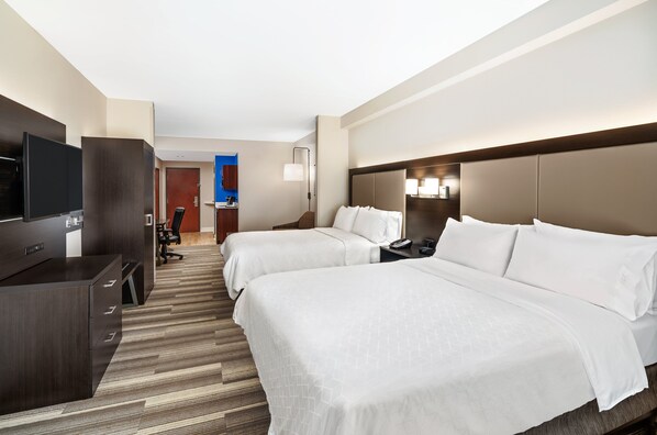 A hotel room with two beds, a desk with a TV, and a bathroom visible through an open door.