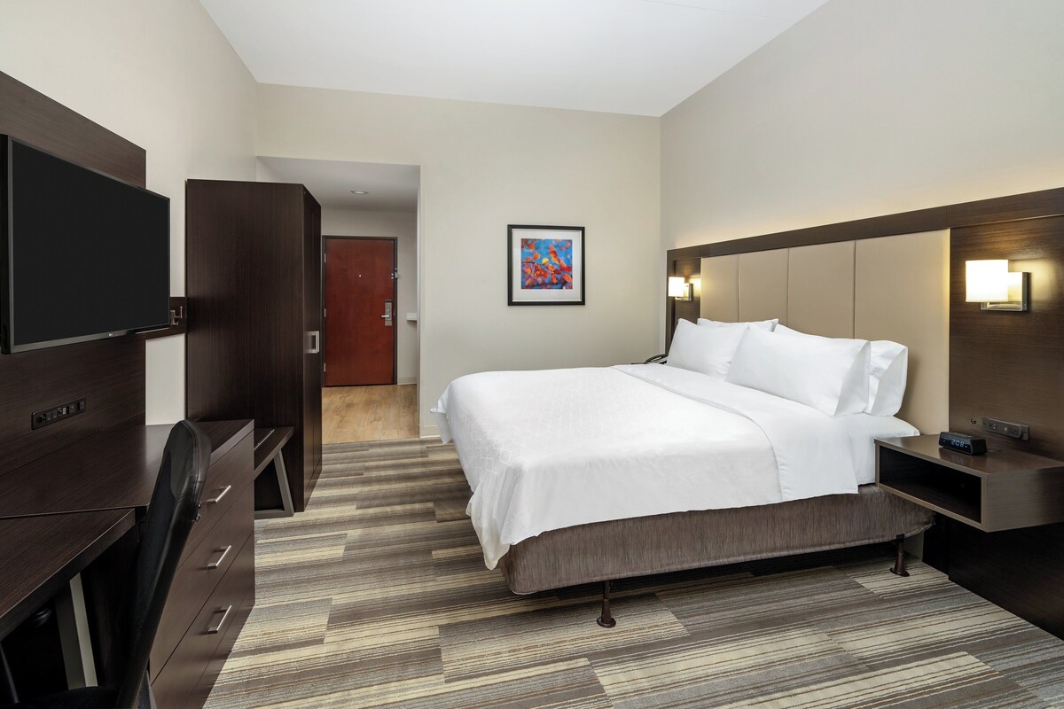 A hotel room with a bed, a desk, a TV, and a painting on the wall.