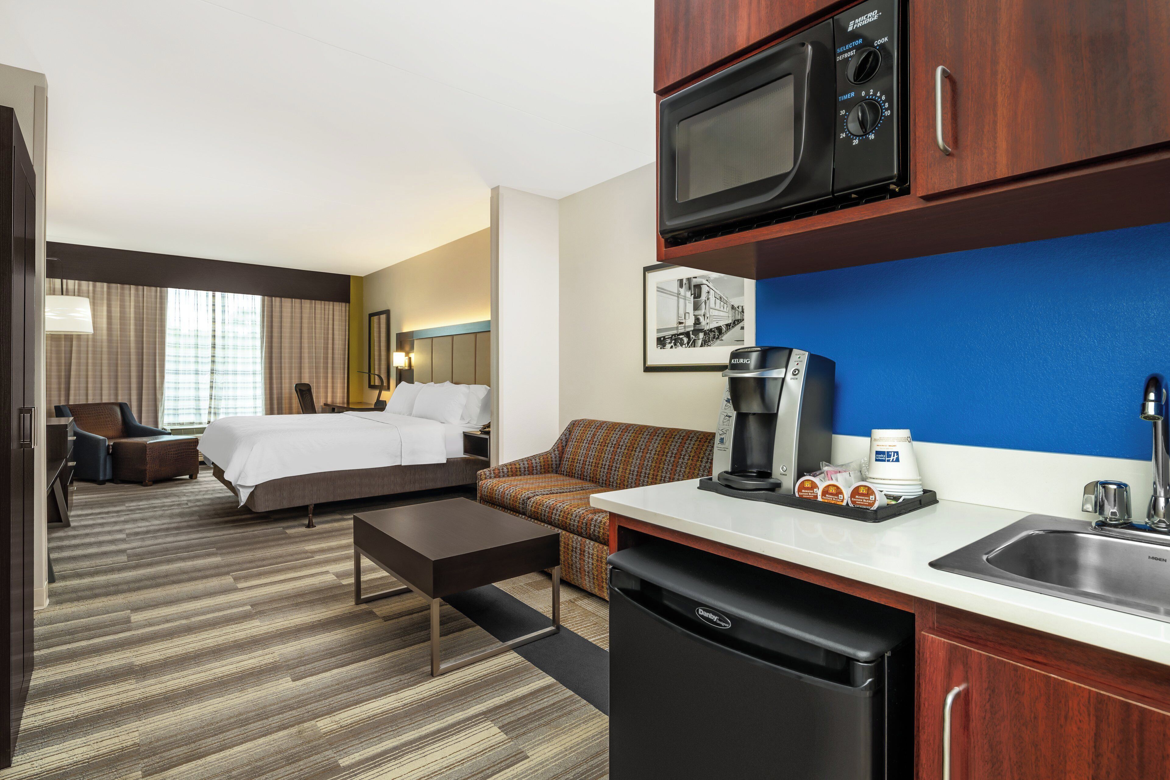 A hotel room with a bed, a sofa, a coffee machine, a microwave, and a sink.