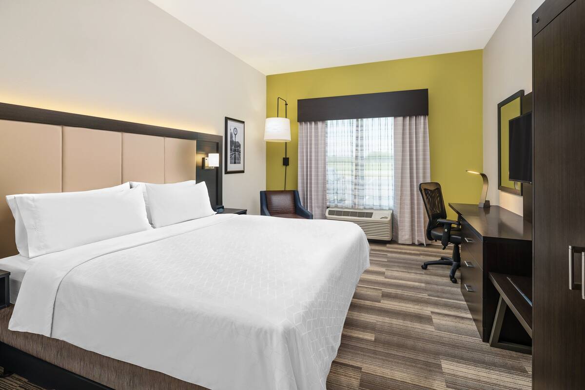Een hotelkamer met een groot bed, een bureau, een stoel, een televisie en een raam met gordijnen.