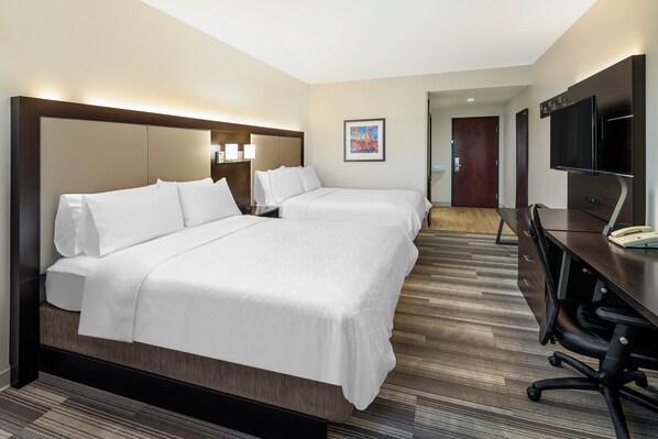 A hotel room with a large bed, a desk, a chair, and a television.