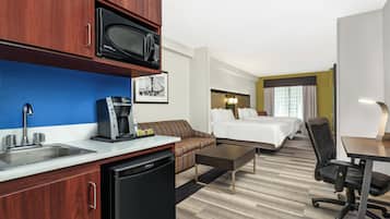Una habitación de hotel con kitchenette, cama, escritorio y silla.